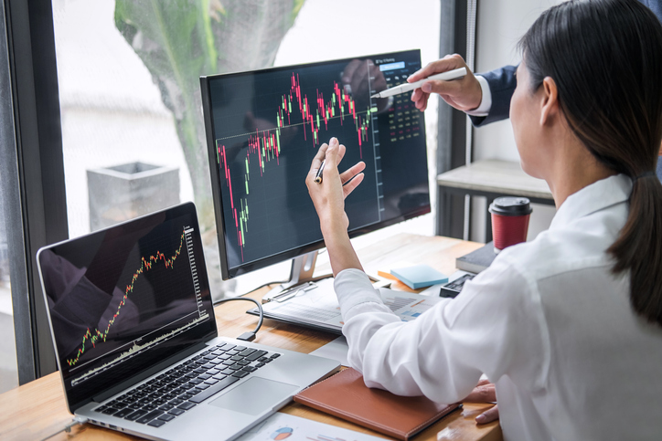 Woman looking at graphs on a computer monitor and laptop