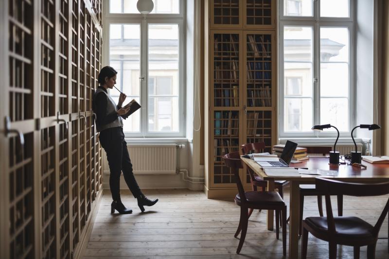 A young woman is leaning against a bookshelf learning about laws in a library. 