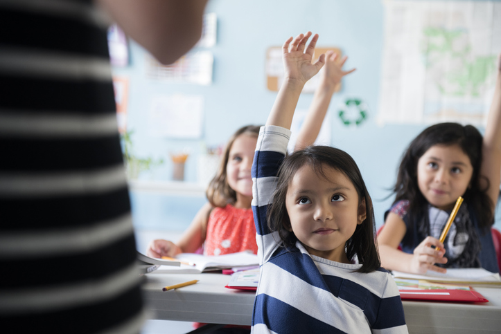 Political campaign questions Little girl in stripes raising her hand in a classroom 
