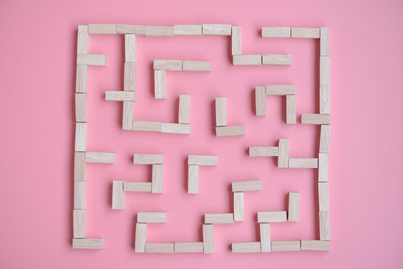 Simple square maze made out of wooden blocks on a pink backdrop