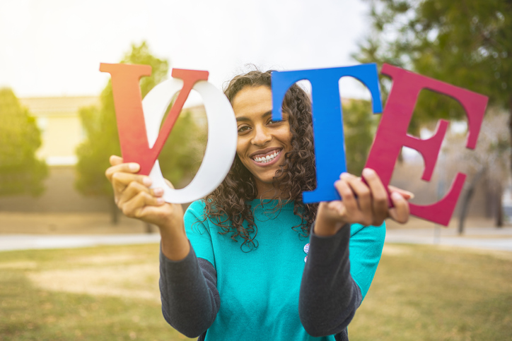 Early Voting- Girl holding up VOTE in letters and smiling at the camera