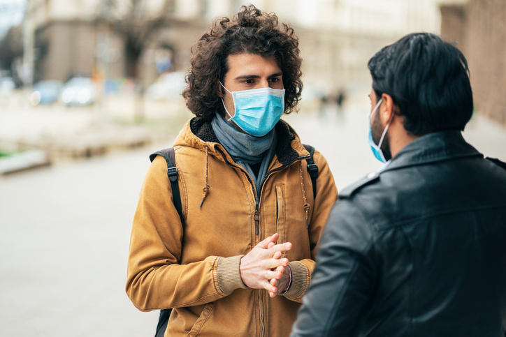 Man with a mask in a tan coat speaking - Field Strategies