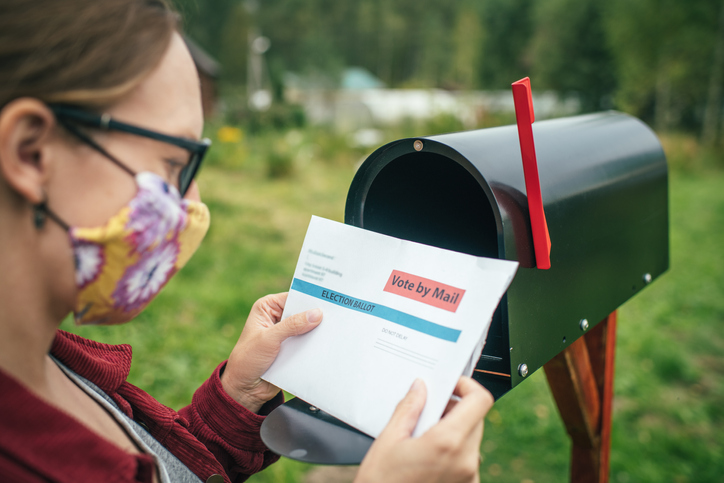 Woman looking at mail in ballot by a mail box - Vote by mail