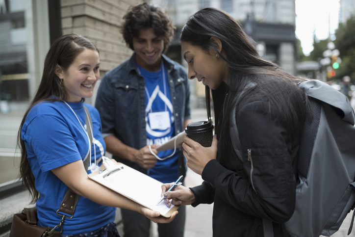 Woman in a blue shirt holding a clipboard while another woman signs her petition