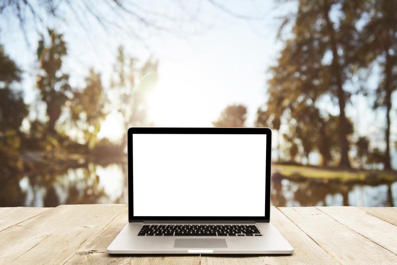 Laptop on a desk in front of a backdrop of water and tress