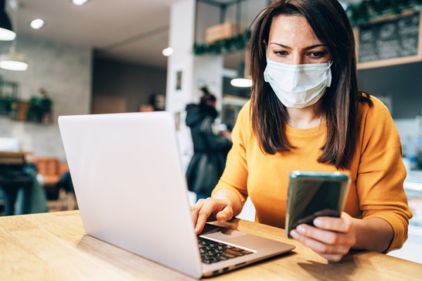Woman with medical mask on looking at phone and laptop