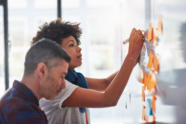 Woman writing on a white board with sticky notes planning out strategy