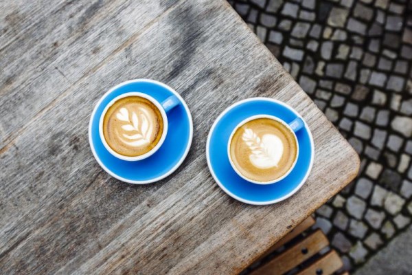 Two latte cups on blue plates sitting on a wooden table. 