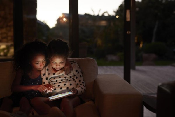 Two girls curled up on the couch looking at an ipad in the dark