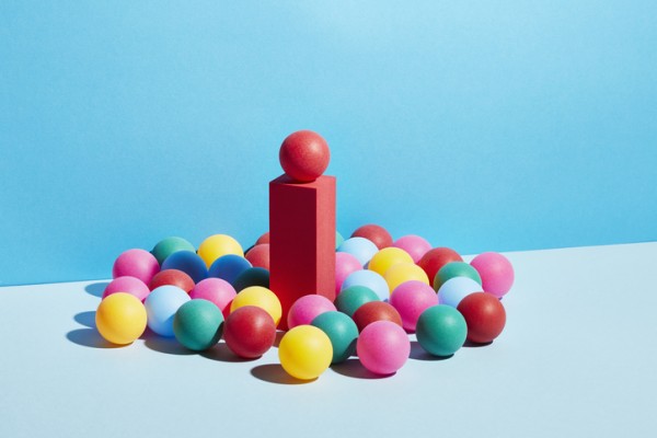 A bunch of colorful balls surrounding a red block with a ball on top of it. 