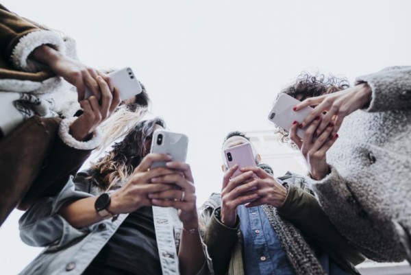 Digital video tips for your ballot measure - Four young adults standing in a circle looking at their phones.