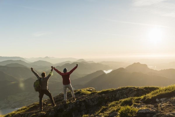 two people at the top of a mountain with their hands up in excitement for their success
