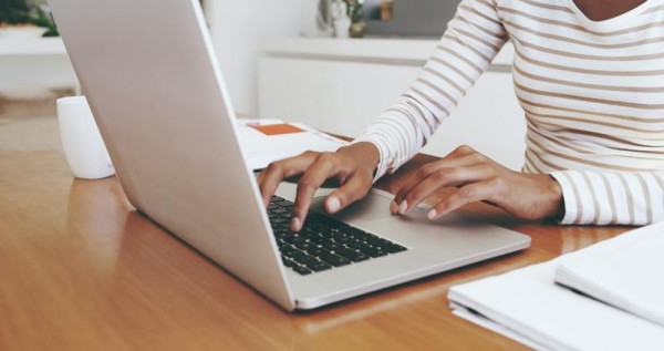 Woman in a striped shirt typing on a silver computer