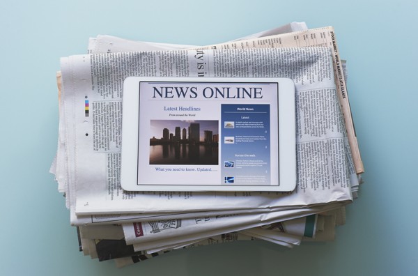 newspaper folded up with a tablet on top of it. Backdrop is light blue. 