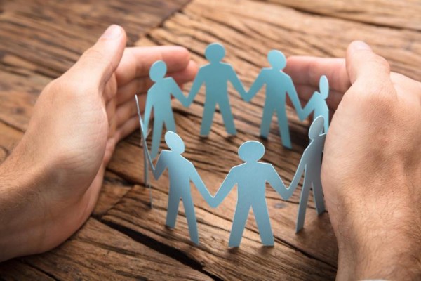 Hands holding a boundary around the paper cut outs of people in a circle